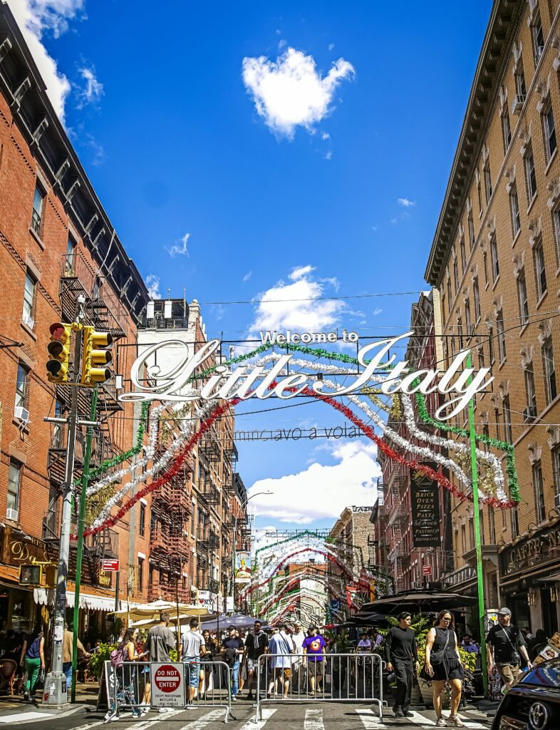 Explore the lively atmosphere of Little Italy, NYC, under a colorful, festive display on a sunny day.